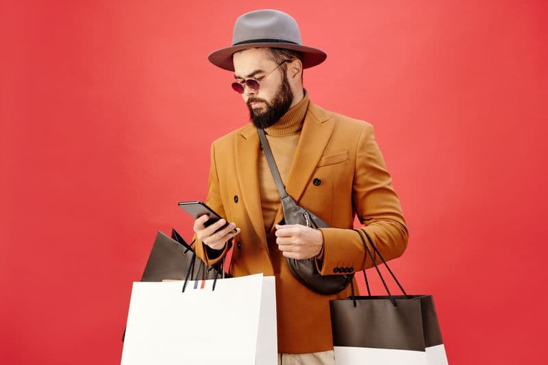 Man in an orange coat and hat carrying shopping bags