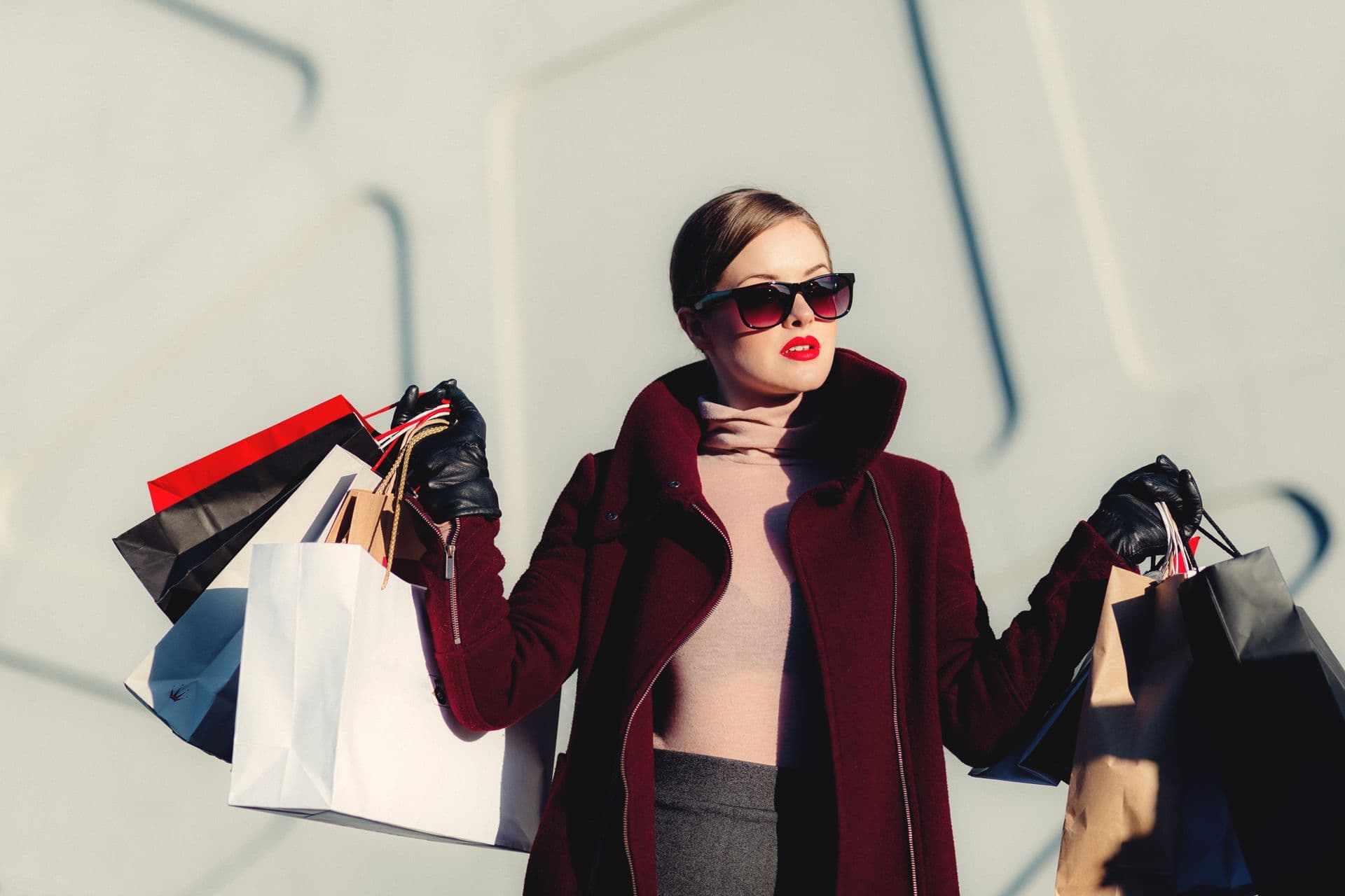 A stylish woman in a burgundy coat carrying shopping bags